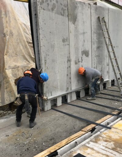 Operai impegnati in lavori di impermeabilizzazione e protezione muri controterra durante fase strutturale di edificio.