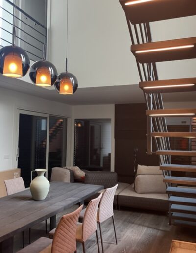 Cucina moderna con isola centrale, illuminazione sospesa e scala a vista, esempio di ristrutturazione interna.