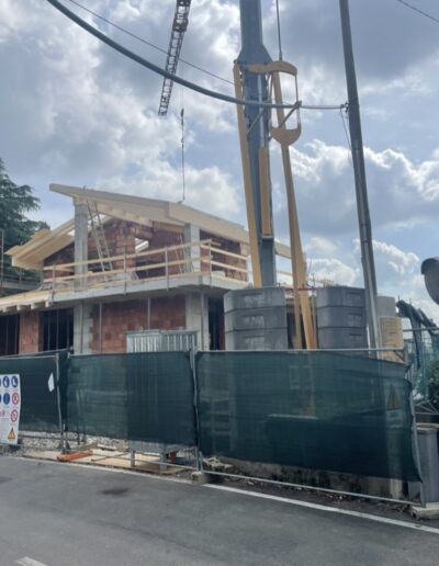 Abitazione in fase di costruzione con ponteggi esterni e struttura al rustico, cantiere edile attivo in contesto urbano.